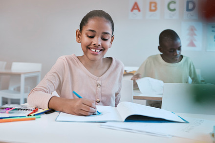 Education, smile and child in classroom learning reading, writing and math in Montessori school in New York. Books, students and happy girl at kid desk in class with notebook studying for future exam, a Photo by Peopleimages.com