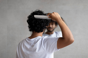 Back view of indian curly man combing hair standing near mirror in bathroom. Ma, a Person Photo by Prostock-Studio
