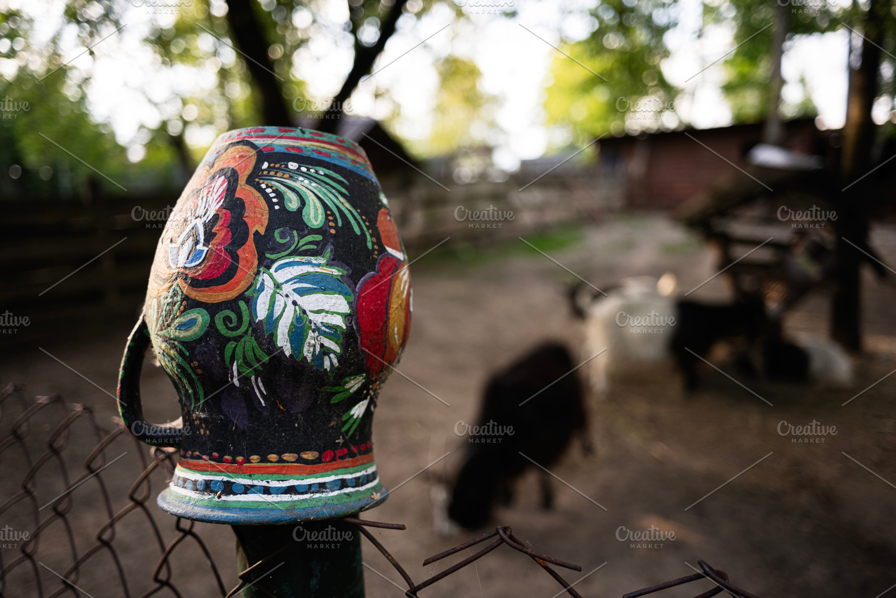 Decorative jug on fence with blurred animals in a rustic outdoor setting, a Photo by AS photostudio