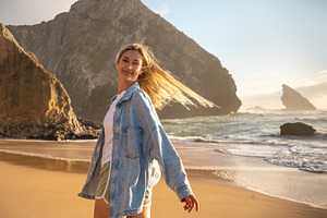 Smiling woman standing against huge rock on seashore at beach, a Photo by andreonegin market