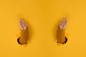 Hands in a yellow sweater pass through holes in yellow paper wit, a Person Photo by ndanko