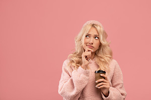 Pensive woman holding takeaway coffee and pondering on offer, looking aside at, a Photo by Prostock-Studio