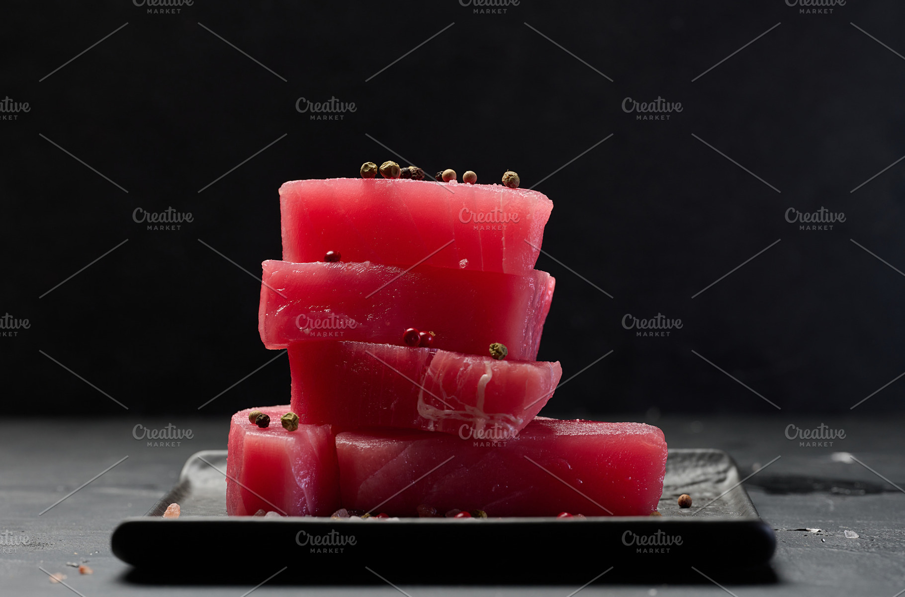 Stack of raw tuna pieces on black plate, black table, a Food & Drink Photo by ndanko