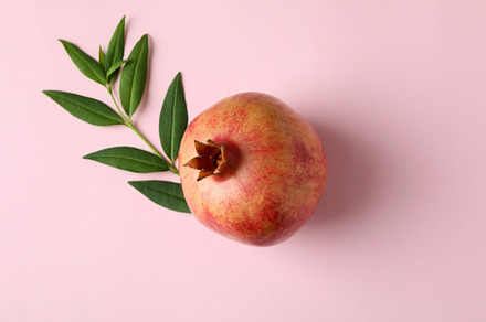 Ripe pomegranate and leaves on pink background, a Food & Drink Photo by AtlasStudio PRO