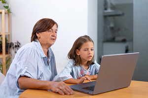 Focused granddaughter and grandmother surfing on laptop at home, a Photo by andreonegin market