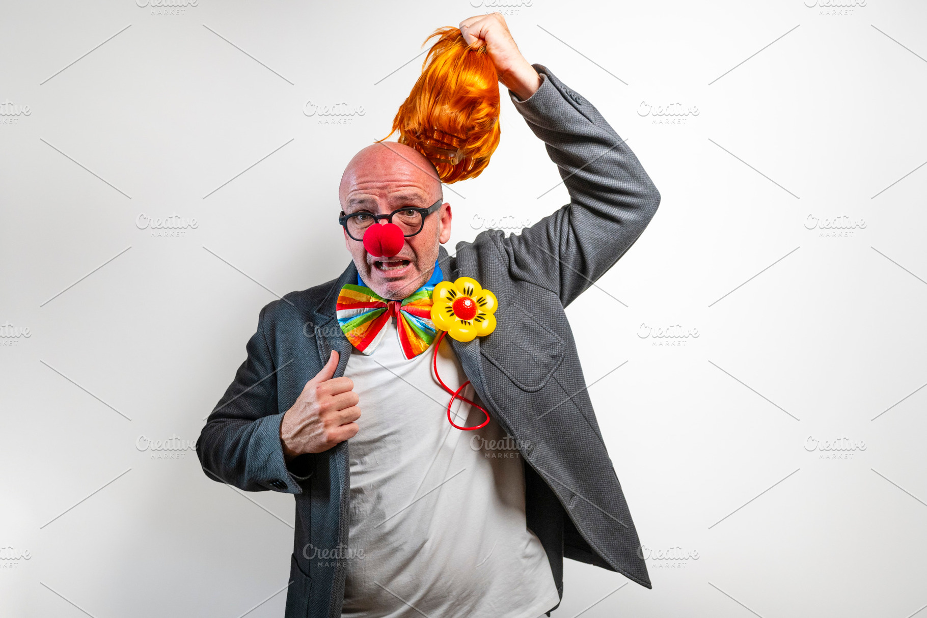 Man removing orange wig revealing bald head with clown nose, a Person Photo by karrastock