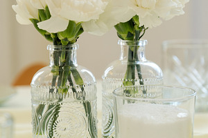 Elegant white carnations in decorative vintage glass bottles on table., a Food & Drink Photo by Rohan Photography