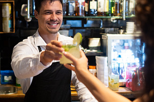 Smiling bartender serving cocktail to customer at modern restaurant bar, a Person Photo by etorres69