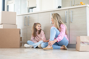 Mother and daughter sitting on kitchen floor among moving boxes in new home, a Person Photo by etorres69