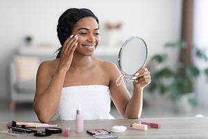 Pretty young black woman applying make up and smiling
