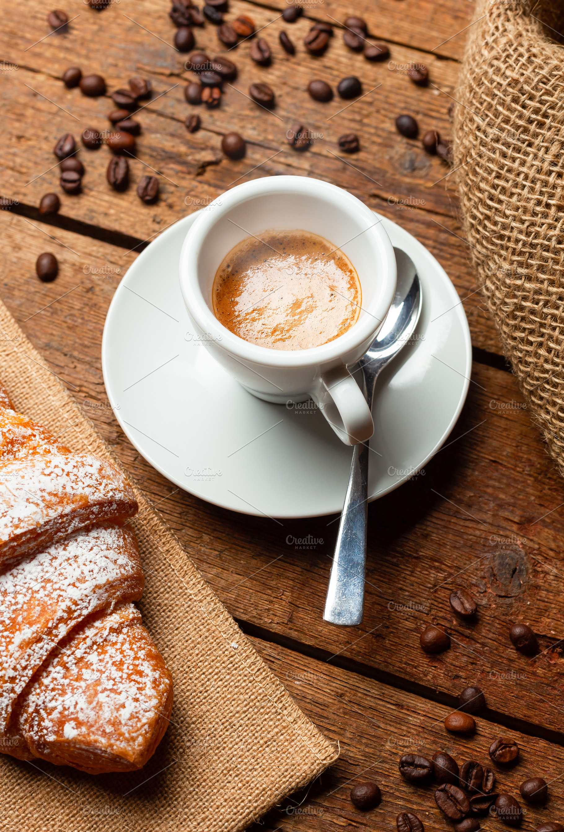 Steaming cup of espresso with croissant and coffee beans on wooden table, a Food & Drink Photo by Antonio Gravante Market