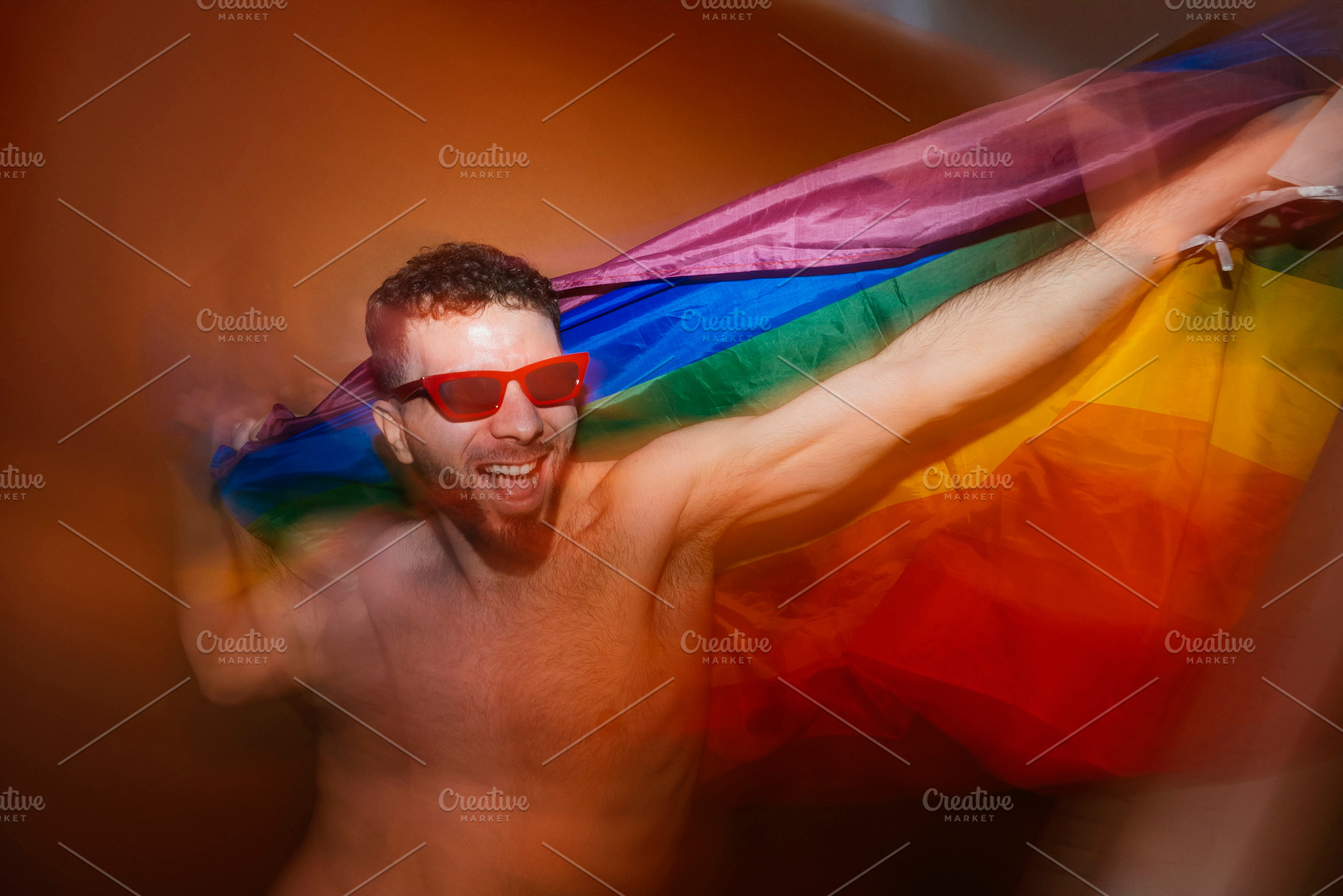Man celebrating pride with rainbow flag and red sunglasses, a Photo by karrastock