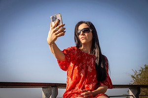 Young woman in a red off-shoulder dress and sunglasses taking a, a Person Photo by Imaginarium