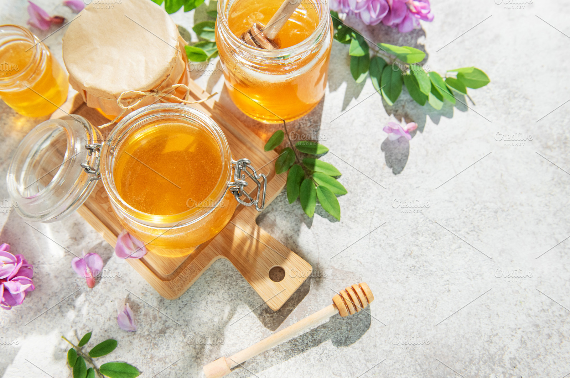 Golden acacia honey in jars with dipper, flowers, a Food & Drink Photo by Olena Rudo