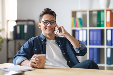 Handsome Young Man Enjoying Phone Conversation During Coffee Break In Office