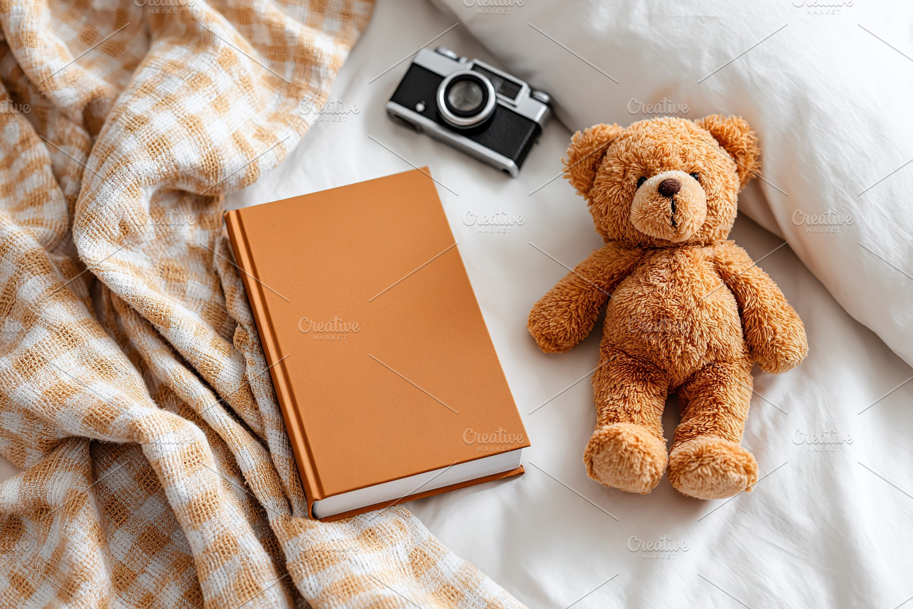 Blank hardcover book on bed alongside teddy bear and vintage camera in cozy set, a Photo by AlyaAnd
