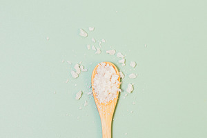 Sea salt crystals in wooden spoon on green background