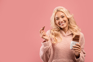 I love cocolate. Pretty lady holding chocolate bar and smiling at camera, stand, a Photo by Prostock-Studio