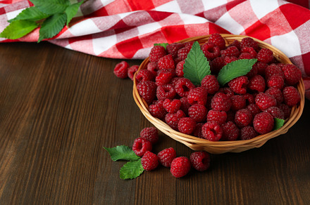 Raspberries in a wicker bowl and a tea towel on a wooden table, a Food & Drink Photo by AtlasStudio