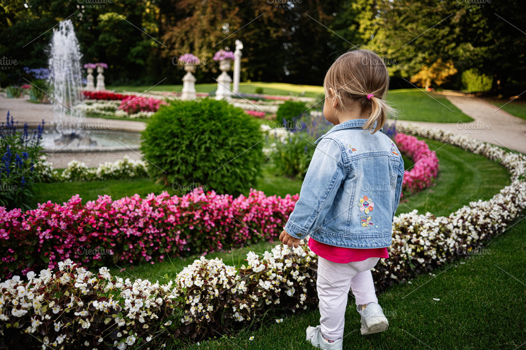 Young child exploring a vibrant garden with flowers and fountain in Lancut, Pol, a Photo by AS photostudio