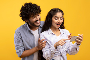 Excited indian couple looking at smartphone screen, using new app or reading co, a Photo by Prostock-Studio