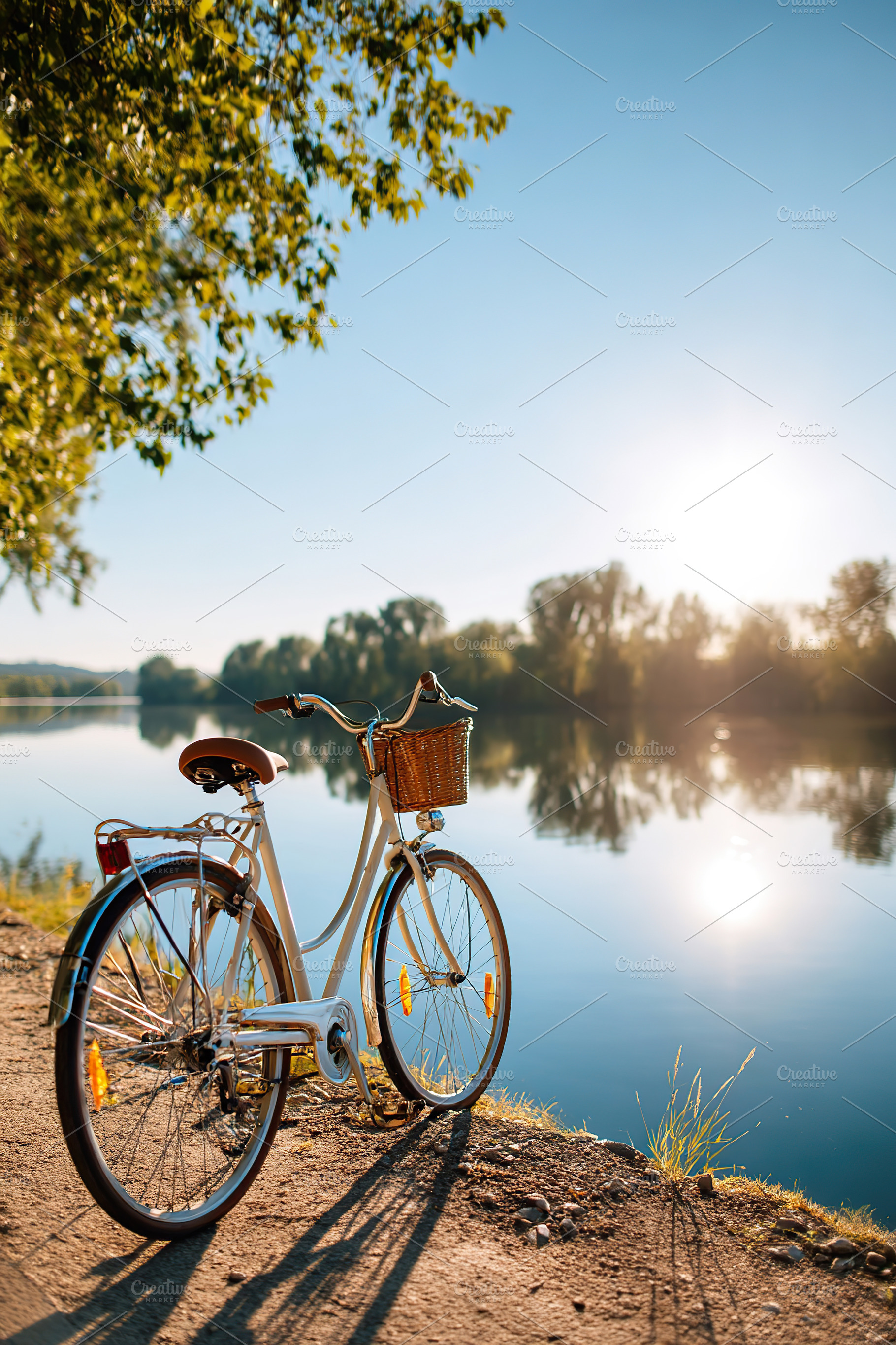 Parked bicycle by a tranquil lake under the clear blue sky at golden hour, a Transportation Photo by AlyaAnd