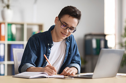 Young Male Office Employee Taking Notes While Working With Laptop In Office, a Photo by Prostock-Studio