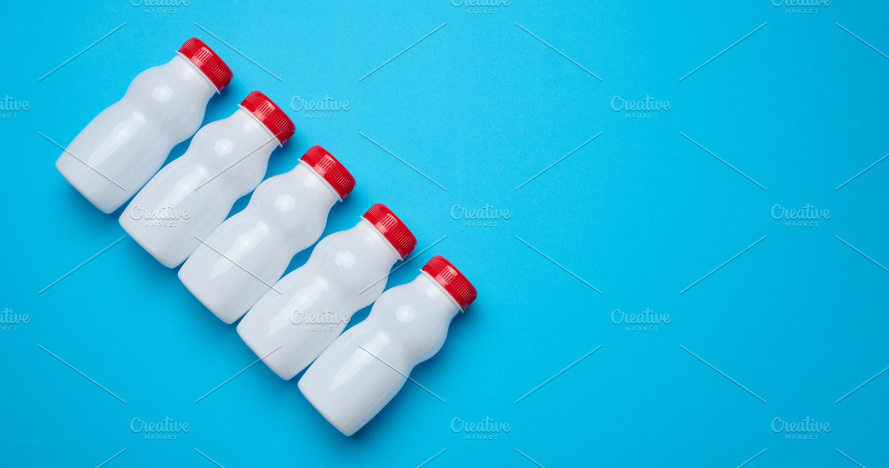 White plastic bottles with red caps for dairy products on a blue, a Food & Drink Photo by ndanko