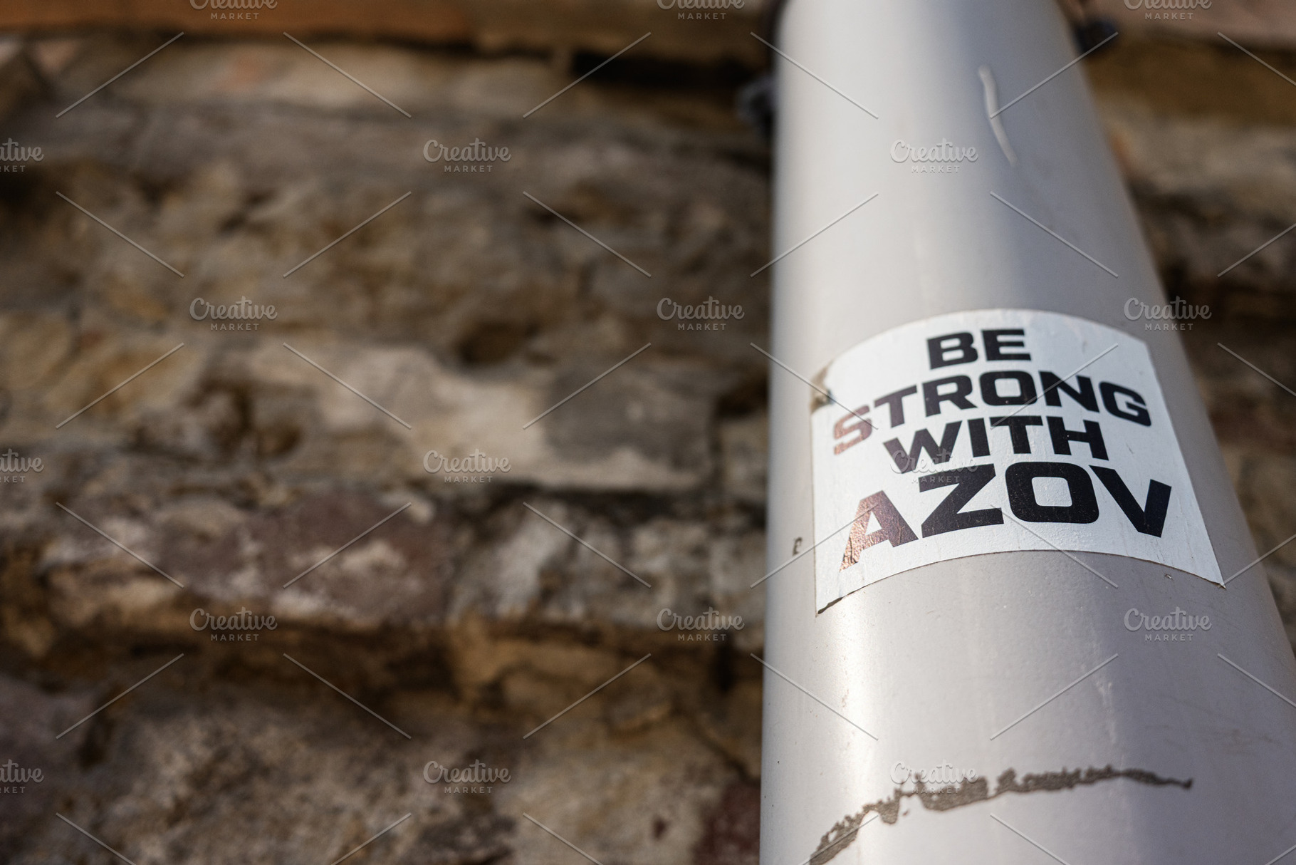 Sticker supporting Azov Brigade displayed on a metallic pipe against a brick wa, a Photo by AS photostudio