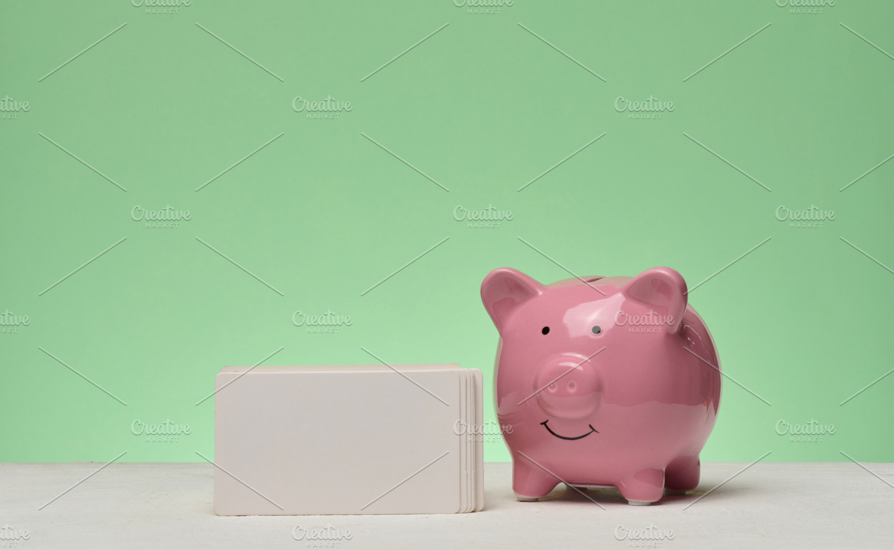 Pink ceramic piggy bank and stack of white business cards on gre, a Business Photo by ndanko