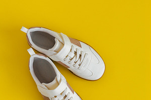 White kids sneakers,yellow backgroun, a Beauty & Fashion Photo by Kolomiyets Viktoriya