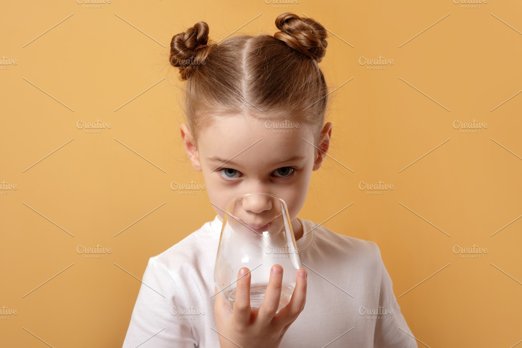Young girl with twin buns drinks from a clear glass against a vi, a Person Photo by Ales Munt