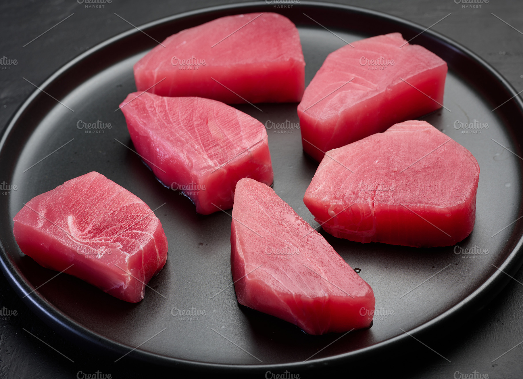 Raw tuna pieces on a black round plate, top view, a Food & Drink Photo by ndanko