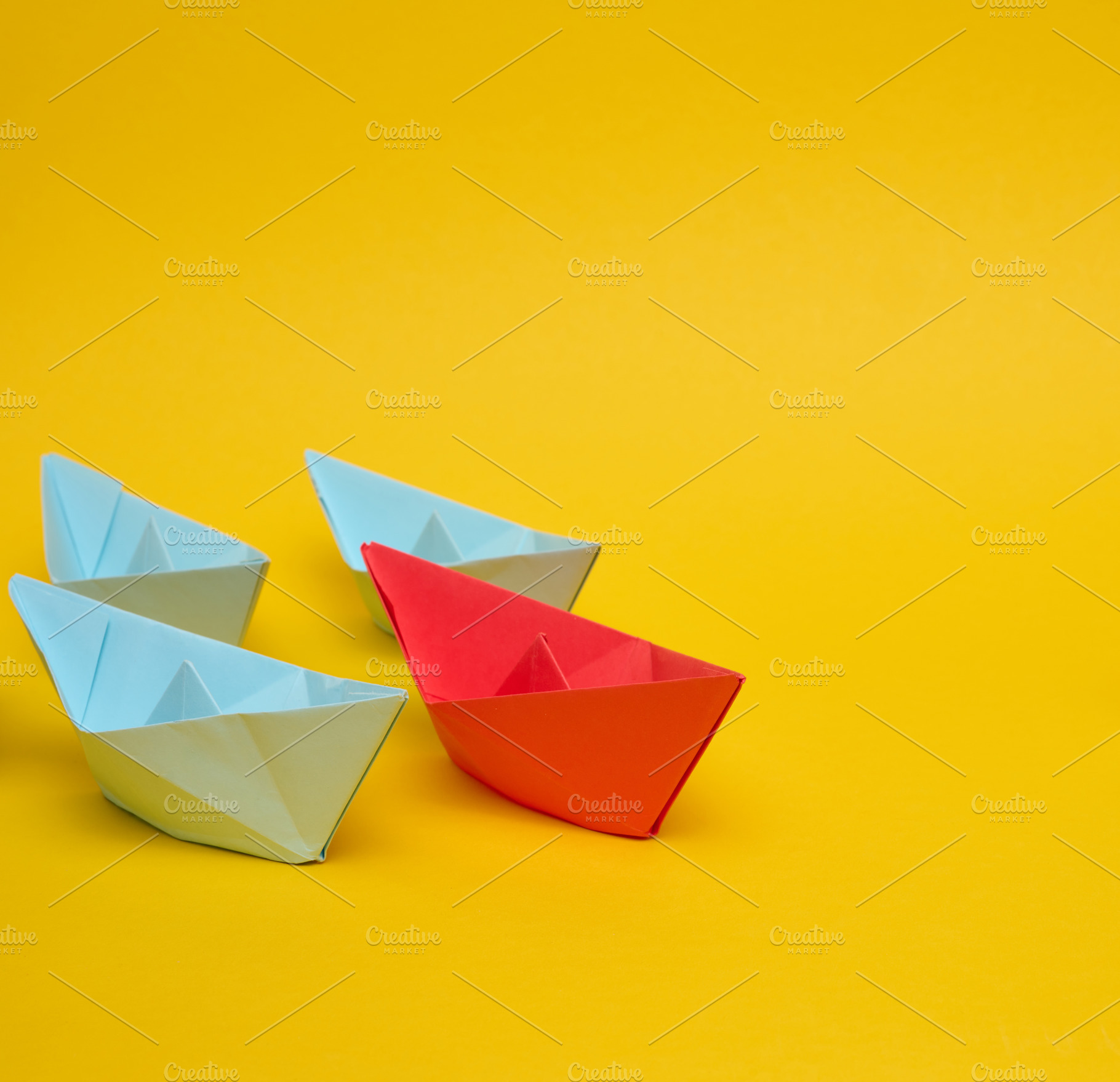 A red paper boat leads a group of three blue boats against a bri, an Abstract Photo by ndanko