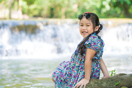 little girl sitting on the root tree and enjoying waterfall land, a Person Photo by Casanowe-studio