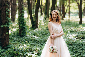 Blonde bride in a light coral dress in a green forest, a Person Photo by Weddings, People, Travel