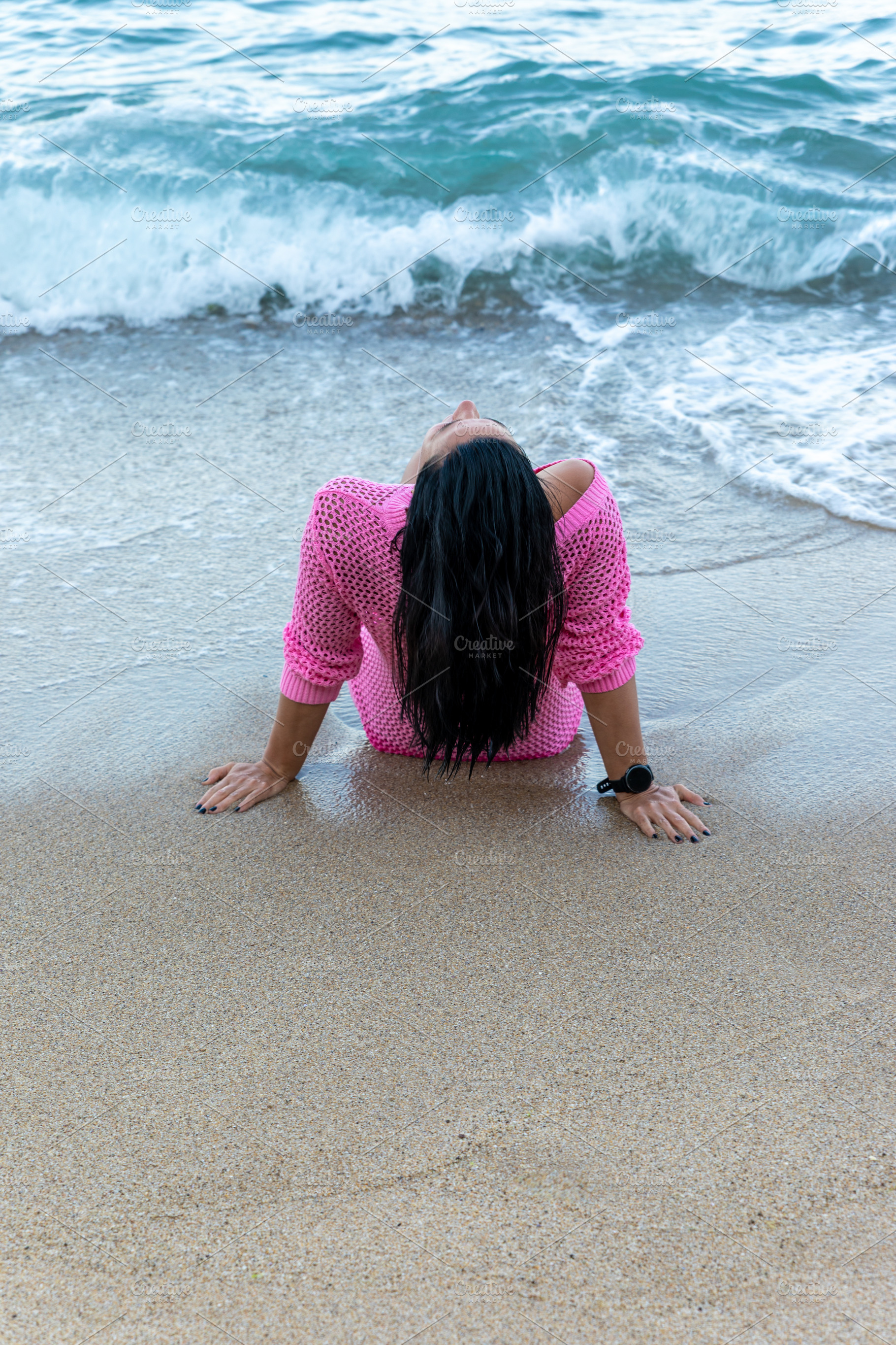 Back view of woman in pink sweater sitting on shore with waves, enjoying the pe, a Person Photo by Ales Munt