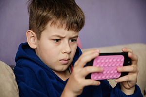 Young boy engrossed in watching a video or playing a game on a smartphone., a Person Photo by Rohan Photography