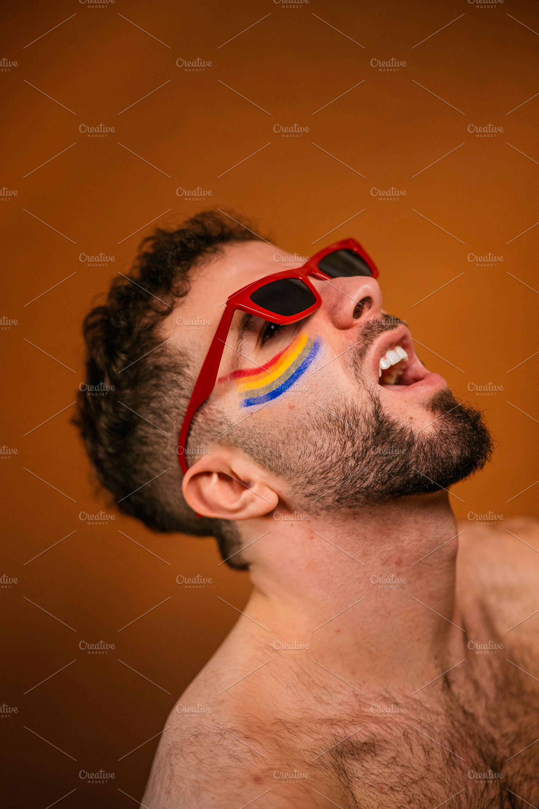 Man expressing pride wearing rainbow face paint and red sunglasses, a Photo by karrastock