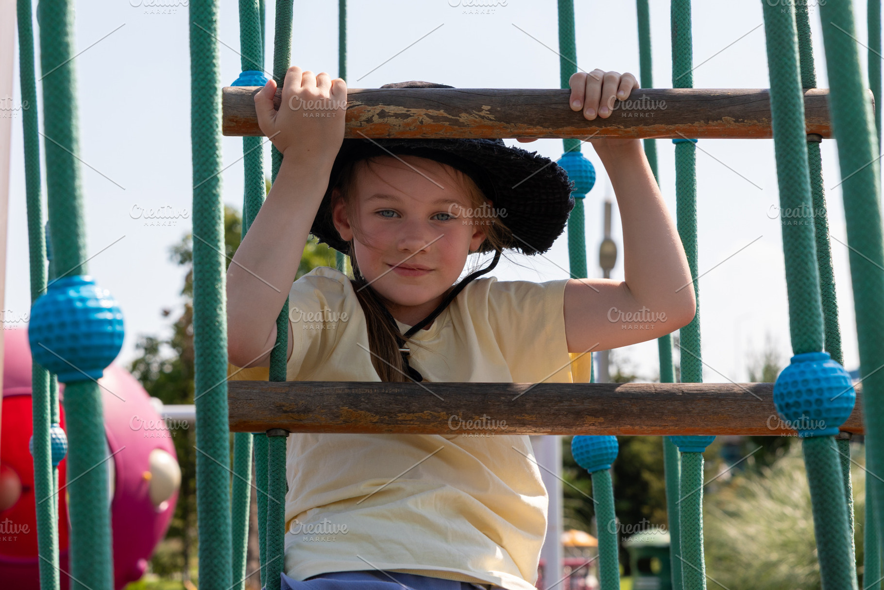 Young girl climbing on a rope ladder at a sunny outdoor playground, wearing a b, a Person Photo by Ales Munt