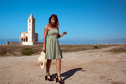 a young girl posing in a hat in the desert with a church in the background., a Beauty & Fashion Photo by YossSabalet